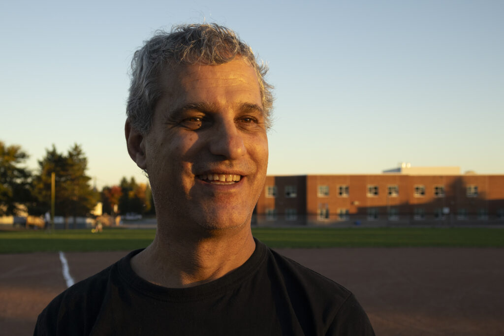 A medium shot of a man smiling at golden hour on a base ball filed